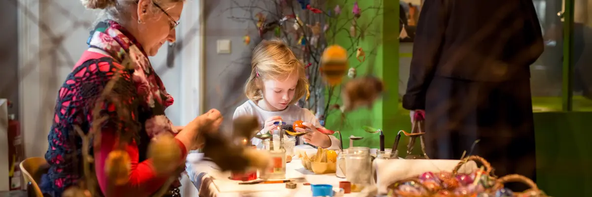 Eine Frau mit Kind an einem Basteltisch, an dem Ostereier bemalt werden.
