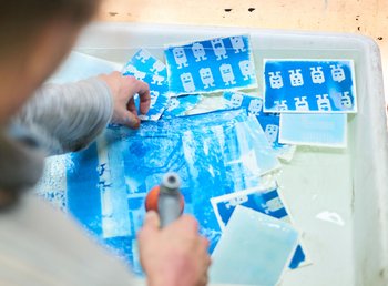 Person arbeitet an einer Wanne, gefüllt mit einer Flüssigkeit und gefärbtem Papier