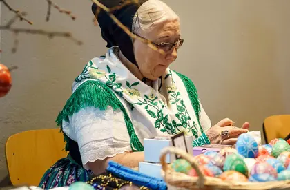 Volkskünstlerinnen zu Ostern im Jägerhof alte Frau in einer Tracht verkauft bemalte Ostereier an einem Tisch