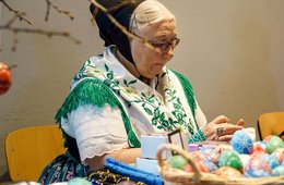 alte Frau in einer Tracht verkauft bemalte Ostereier an einem Tisch