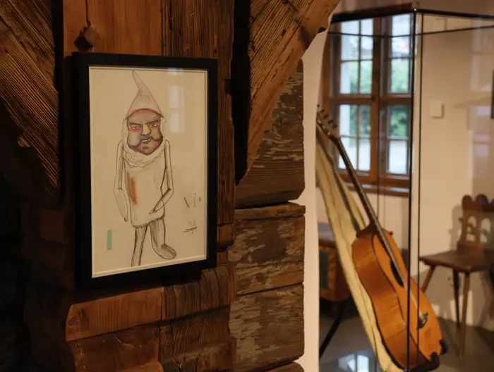 Eine Zeichnung eines Männchens mit spitzer Mütze an einer Wand, im Hintergrund steht eine Gitarre.