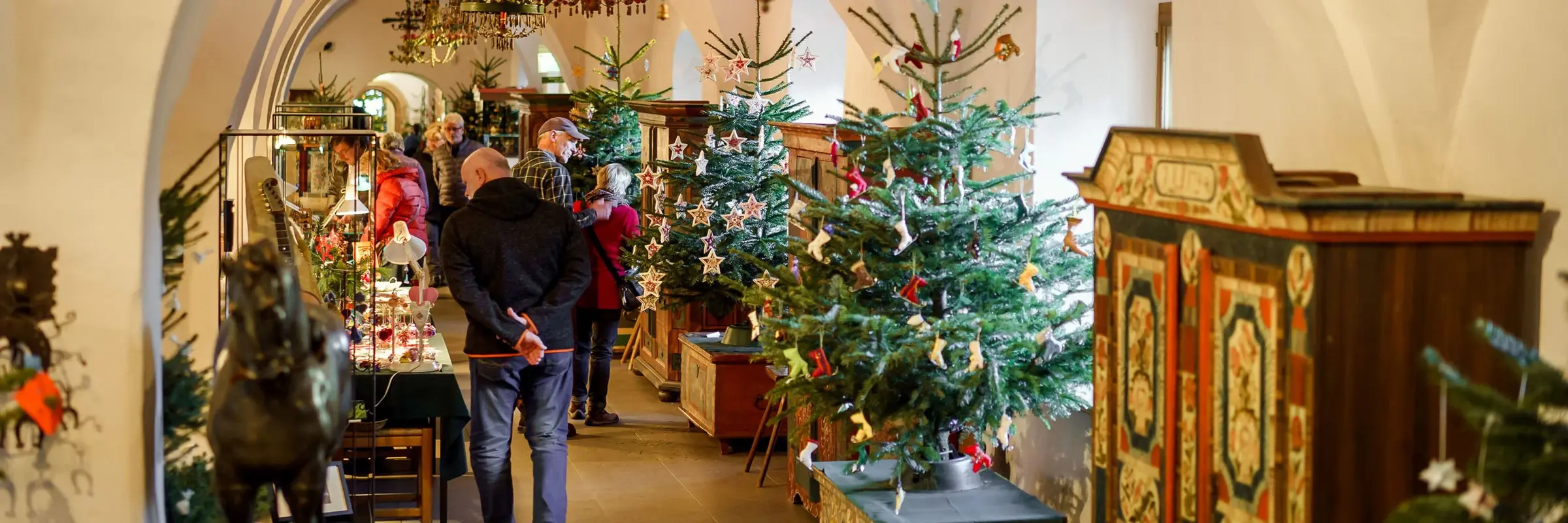 Besucher in einem Raum mit unter anderem verschieden geschmückten Weihnachtsbäumen
