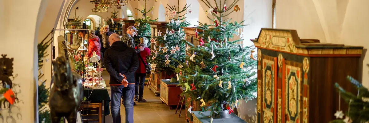 Besucher in einem Raum mit unter anderem verschieden geschmückten Weihnachtsbäumen