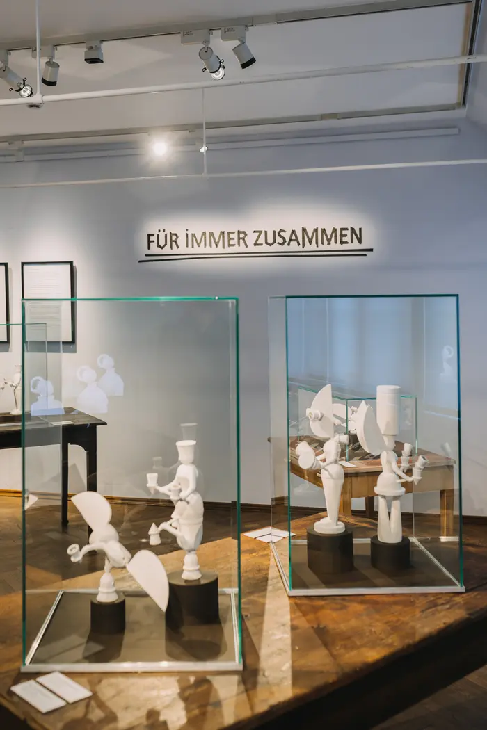 Vitrinen mit Holzfiguren in Ausstellung, Schriftzug "FÜR IMMER ZUSAMMEN" an einer Wand