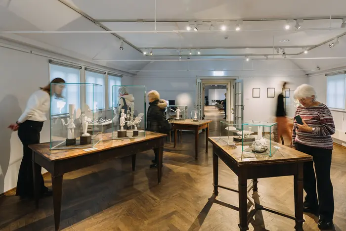 Raumansicht mit Menschen, die auf Holzobjekte in Vitrinen schauen