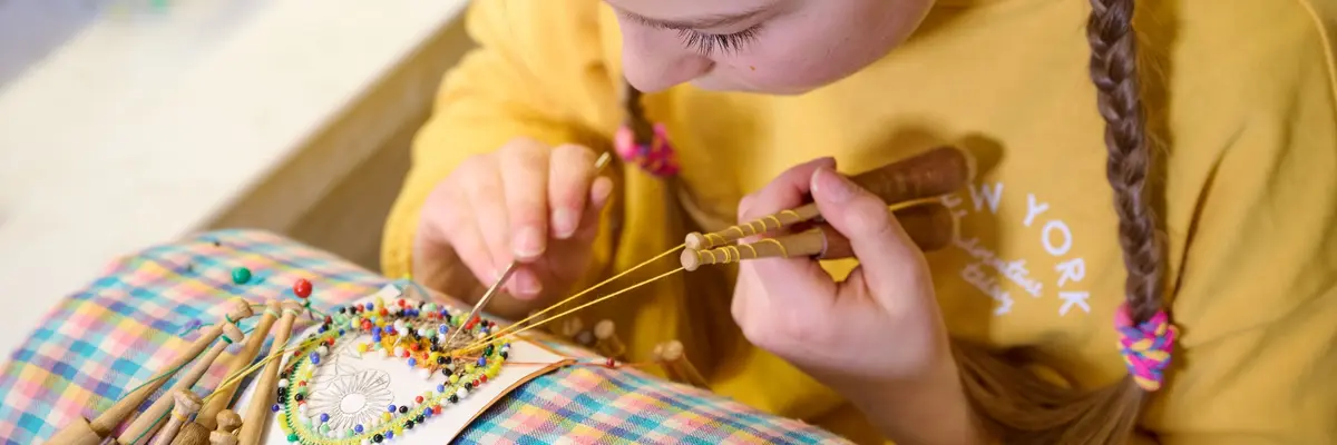 Mädchen sitzt an einem Klöppelstück und macht eine Handarbeit