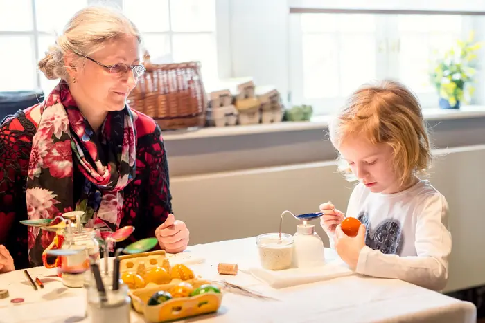 Eine ältere Frau mit Kind, das Eier an einem Tisch bemalt.