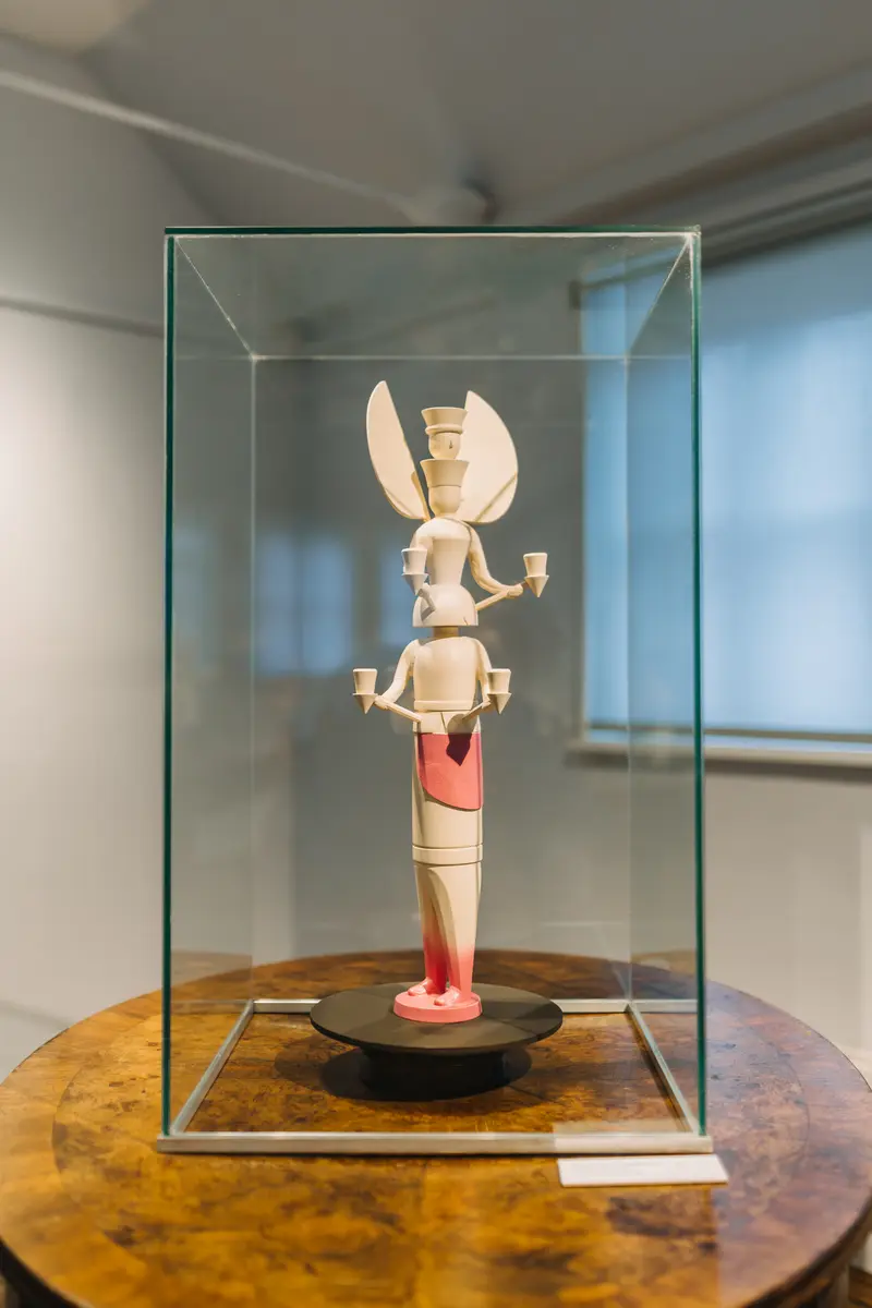 Holzfigur mit pinken Akzenten in Vitrine