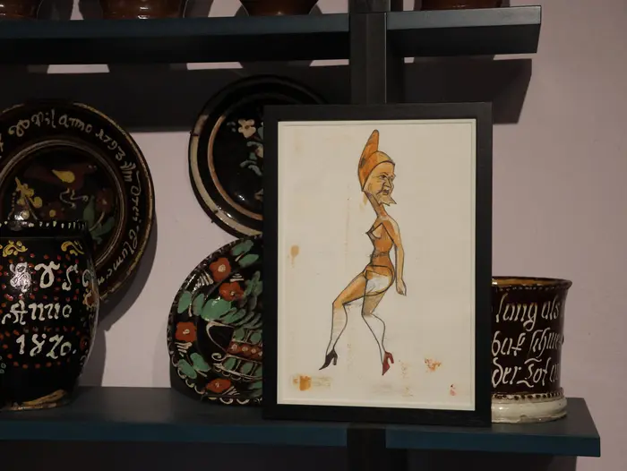 Zeichnung mit kunstvoll bemaltem Geschirr im Hintergrund.