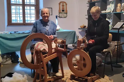 zwei Frauen sitzen an einem Spinnrad