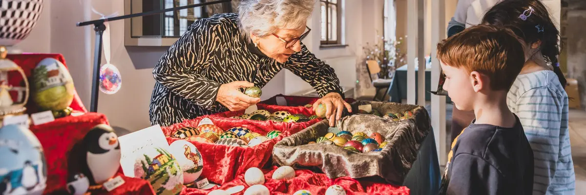 eine Frau zeigt zwei Kindern und einer weiteren Person bemalte Ostereier