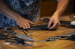Nils Bergauer, Handschuhmacher, Schneeberg Hände an einem Tisch voll mit Stoffen und einer großen Schere