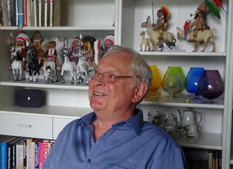 Ein älterer Mann, der vor einem Regal sitzt.