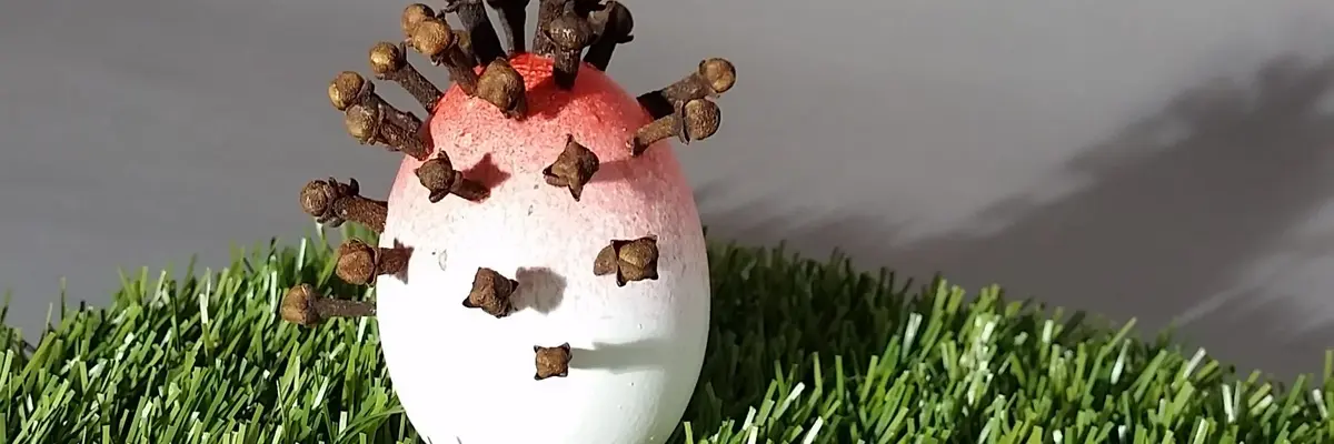 Ein bemaltes Ei auf Kunstgras, in welchem Gewürznelken stecken.