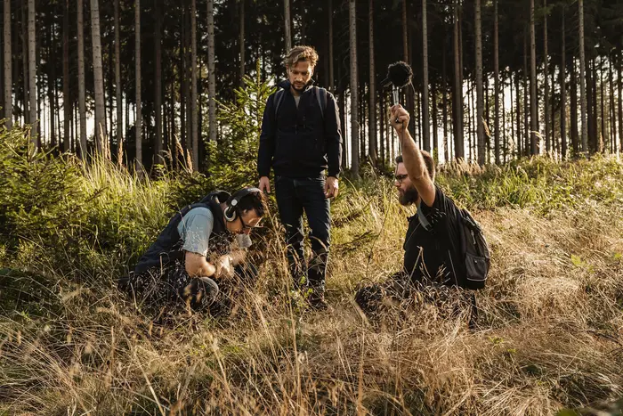 Drei Männer auf einer Waldlichtung, etwas auf dem Boden suchend.