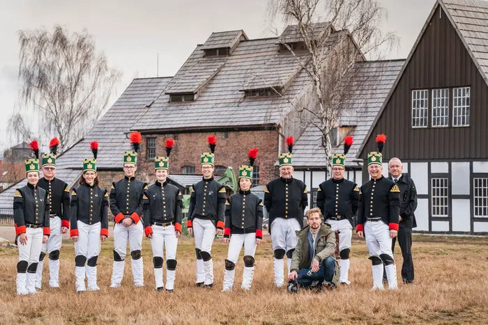 Traditionell gekleidete Menschen auf einer Wiese vor einem Haus.