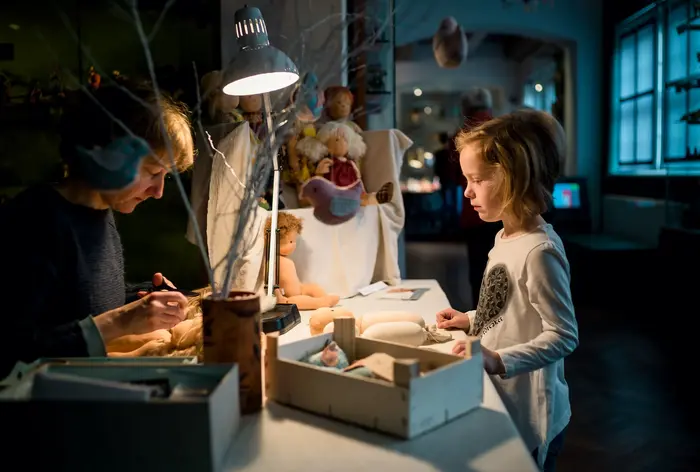 Kind schaut einer Puppennäherin zu