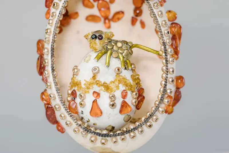 Tier sitzt auf kleinem Ei, dieses wiederum in großem Ei mit weiter Öffnung vorne, alles reich verziert