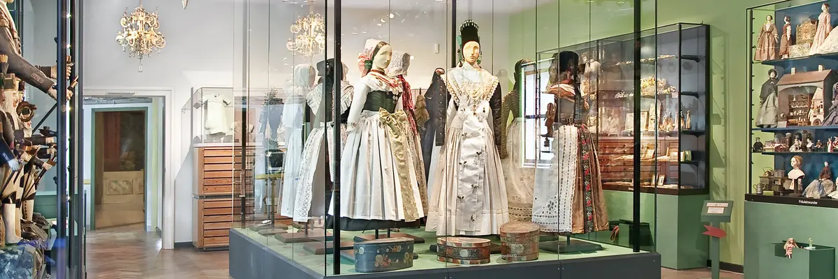 in der Mitte große Puppen in Trachten, drumherum weitere Puppen und Objekte