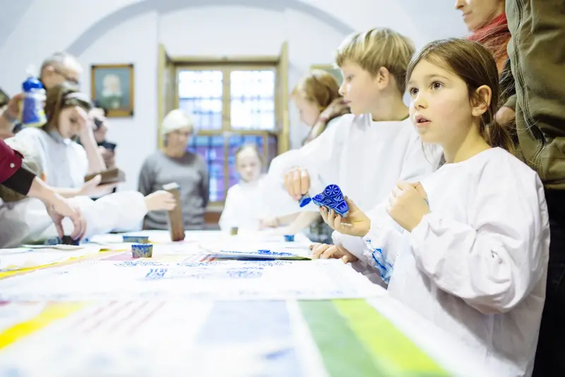 Kinder mit weißen Schürzen, die einen blauen Stempel in der Hand halten