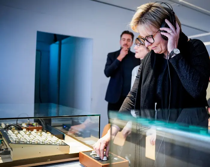 Ausstellungsansicht "Wie klingt Heimat?" Frau hört sich etwas mit Kopfhörern an